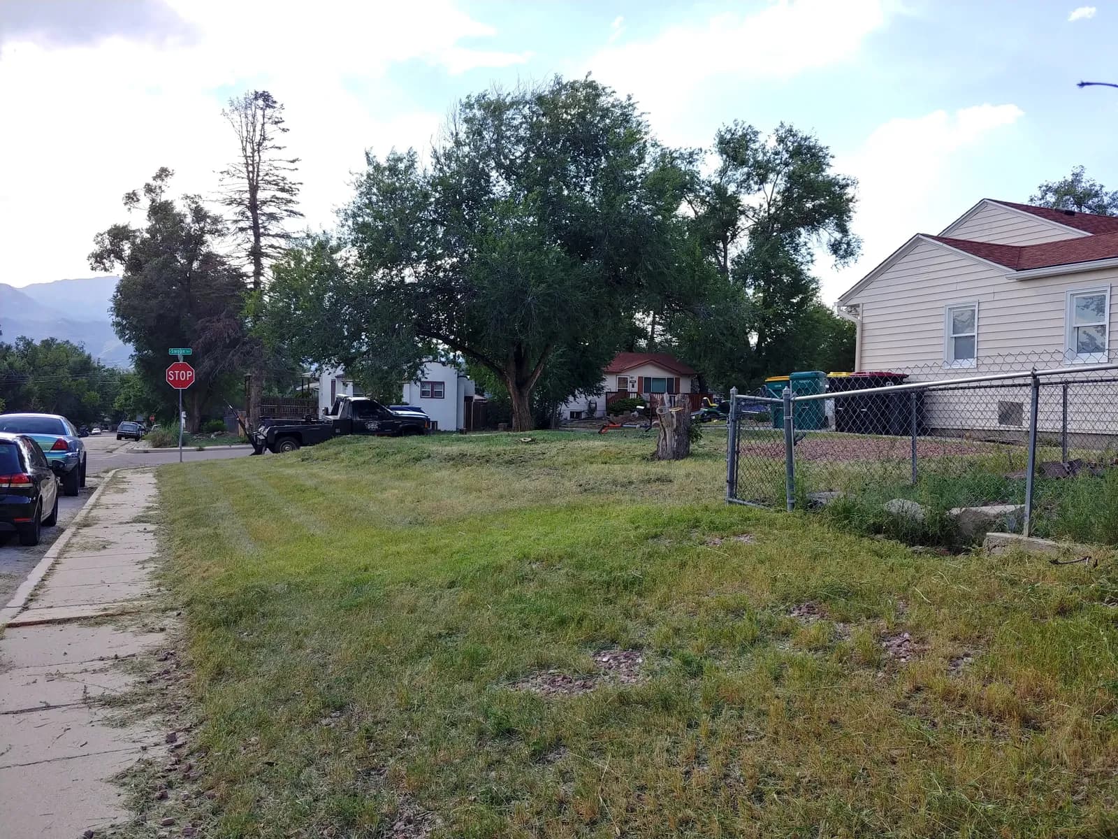 The same corner lot after clearing — weeds gone, grass cut low and edged along the sidewalk