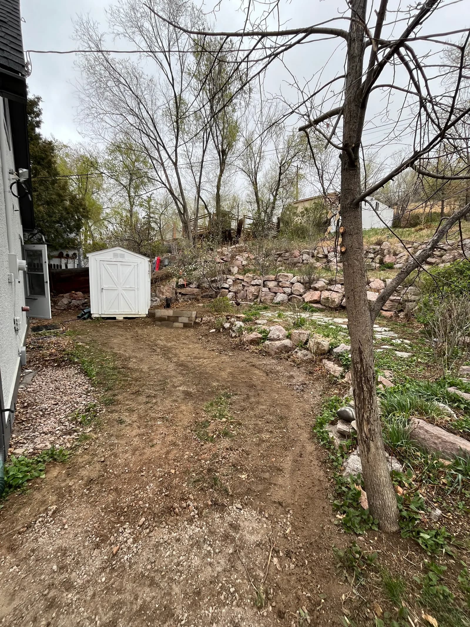 Side yard cleared down to bare ground to open a pathway beside the shed and stone retaining wall