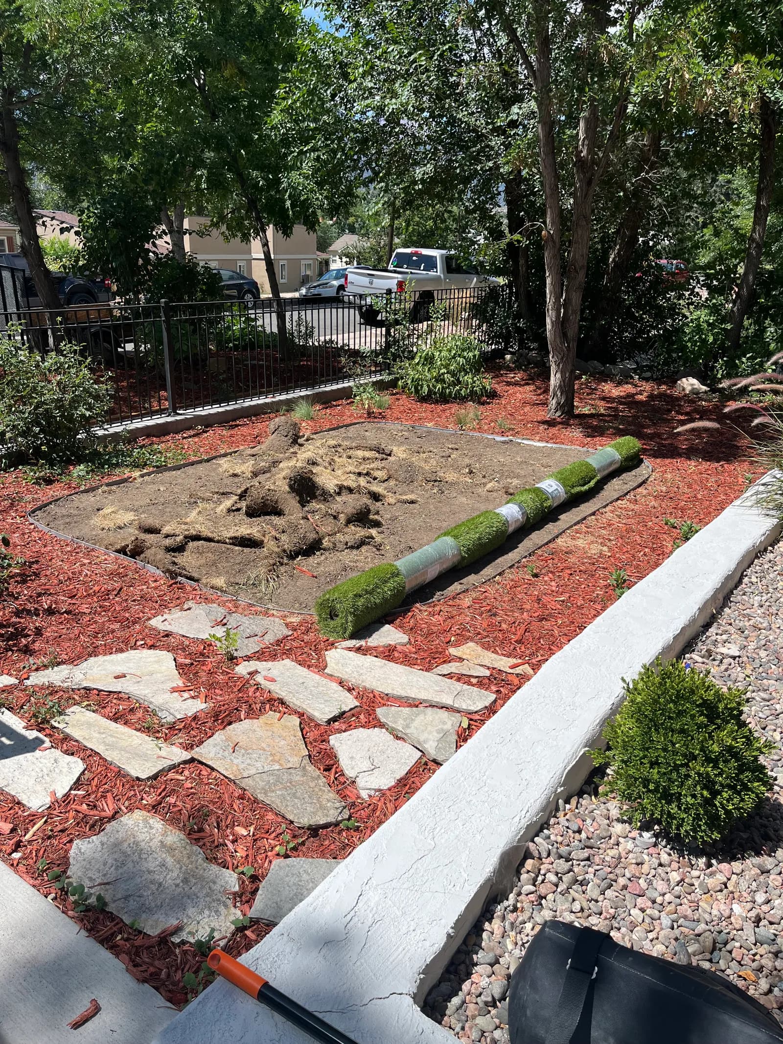 Bare dirt patch edged with red mulch and flagstone, with turf rolls waiting to be laid
